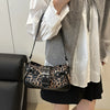 Sac à main imitation cuir léopard porté par une personne en chemise blanche et cardigan gris.