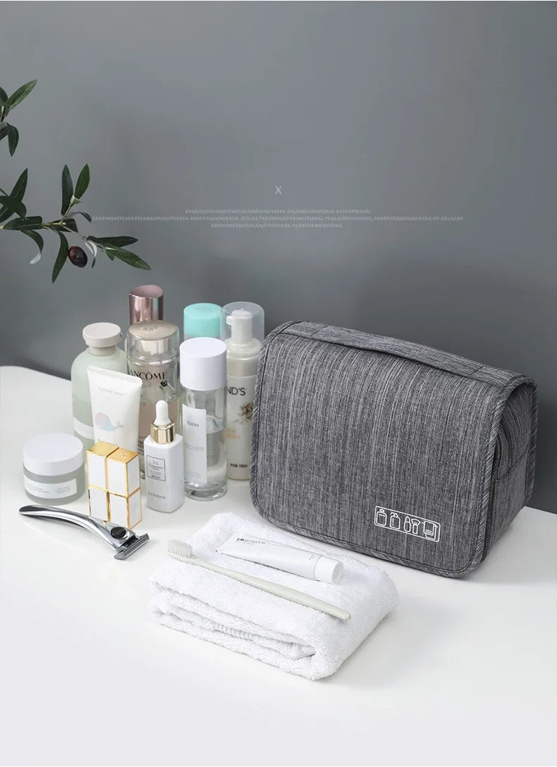 Sac organisateur en tissu gris avec des produits de soin et de beauté, incluant des flacons et une serviette blanche.