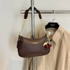 A brown leather shoulder bag with a gold chain and cherry pendant hanging on a metal rack.