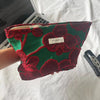 A vibrant green velvet cosmetic pouch with red floral embroidery and a zipper is held against a white background.