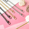 A collection of various metal chain straps in gold and silver tones laid out on a pink surface.