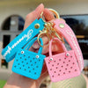 A hand holds a silicone heart beach bag keychain in pink and blue colors.