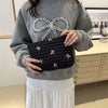A person holds a black embroidered makeup pouch with a zipper against a gray sweater and white skirt.