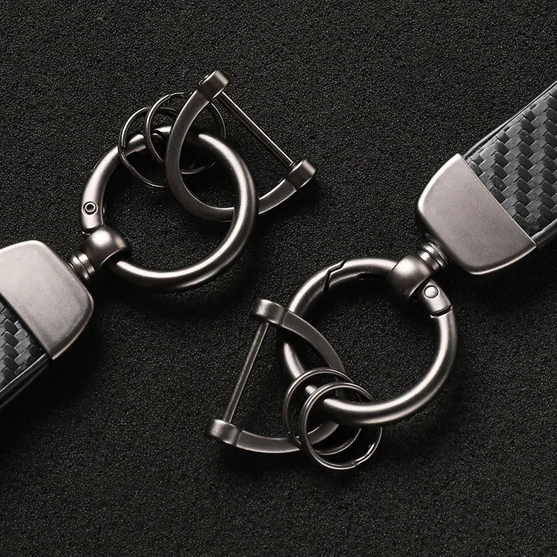 A close-up of a silver carbon fiber leather keychain with a split ring and clasp.