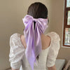 A woman with dark hair wearing a white blouse and a lavender silk bow tied in her hair.