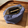 Pochette à motif à carreaux bleu marine avec fermeture éclair dorée contenant un produit cosmétique noir sur une surface en b