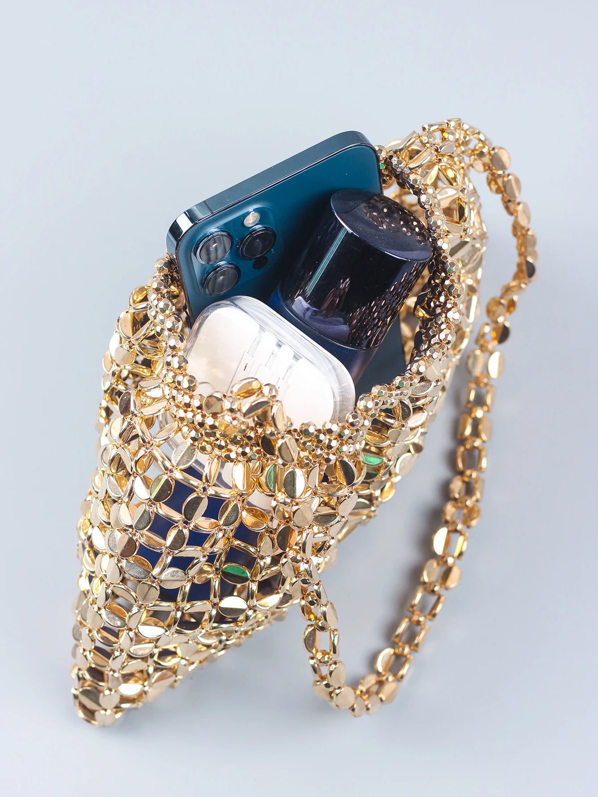 A handmade dumpling bag made of silver and gold beads, holding a smartphone and a clear container.