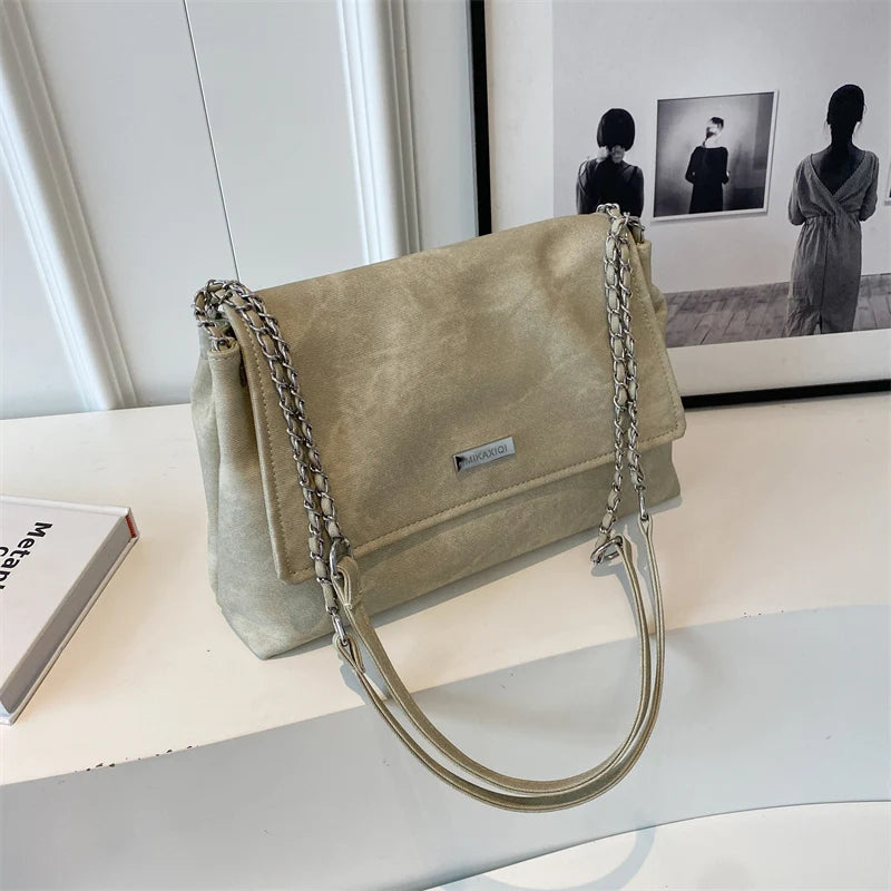 Bolso de cuero retro beige con cadena, apoyado sobre una superficie blanca.