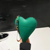 Una mano sostiene un monedero de cuero verde con forma de corazón contra un fondo oscuro.