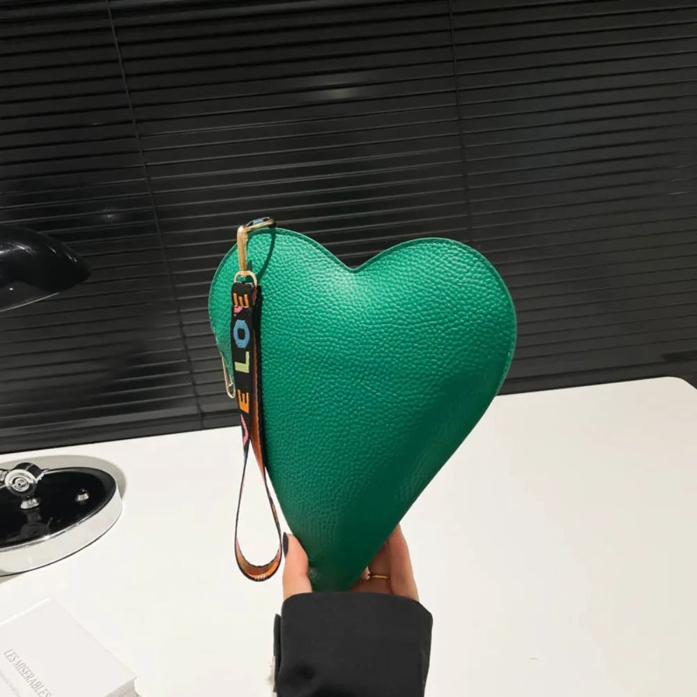 Una mano sostiene un monedero de cuero verde con forma de corazón contra un fondo oscuro.