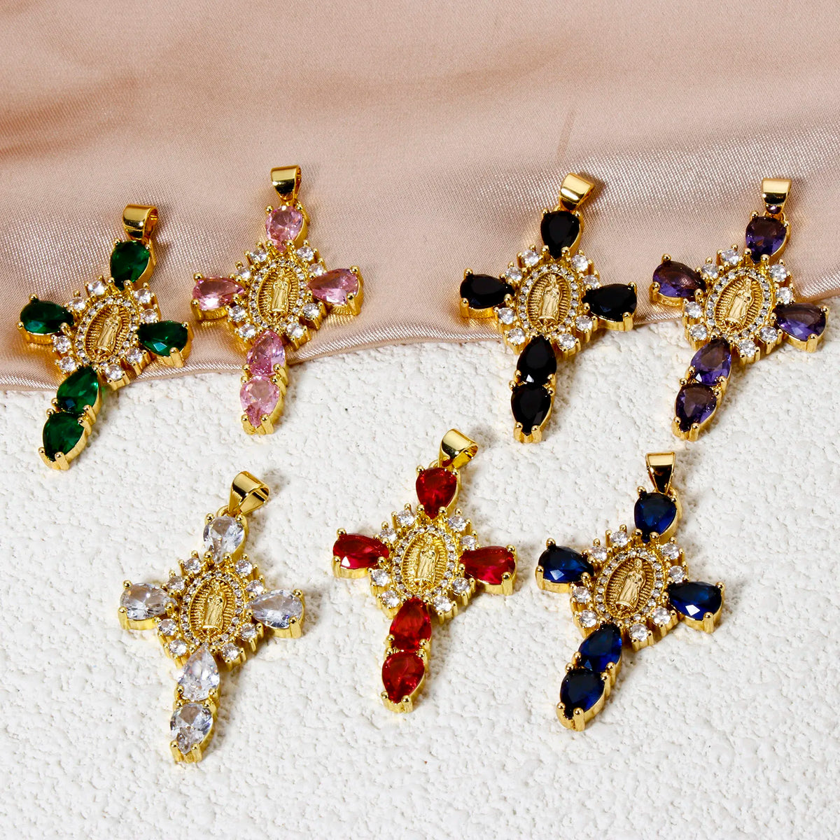 A collection of gold-plated cross and Virgin Mary charm pendants featuring various colored gemstones like pink, green, black,