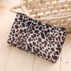 A leopard print zippered cosmetic bag resting on a light wooden surface next to a woven basket.