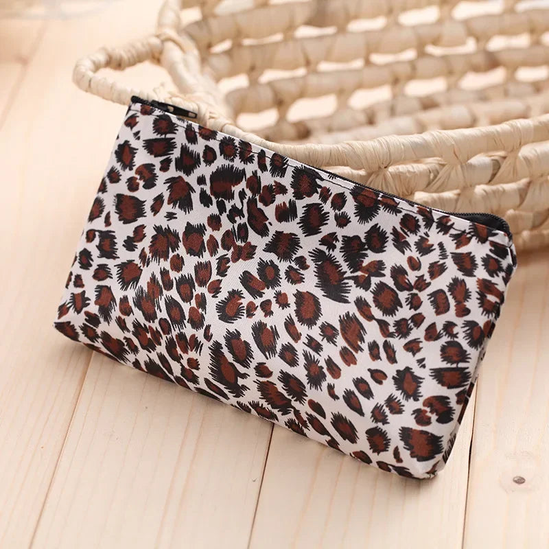 A leopard print zippered cosmetic bag resting on a light wooden surface next to a woven basket.