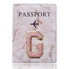 Funda de pasaporte de cuero marmolado rosa con una inicial G dorada y un símbolo de avión.