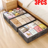 Three foldable under-bed storage boxes filled with soft toys and fabric items placed on a wooden floor.