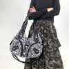 A woman wearing a black top and camouflage skirt holds a leopard print crossbody shoulder bag.