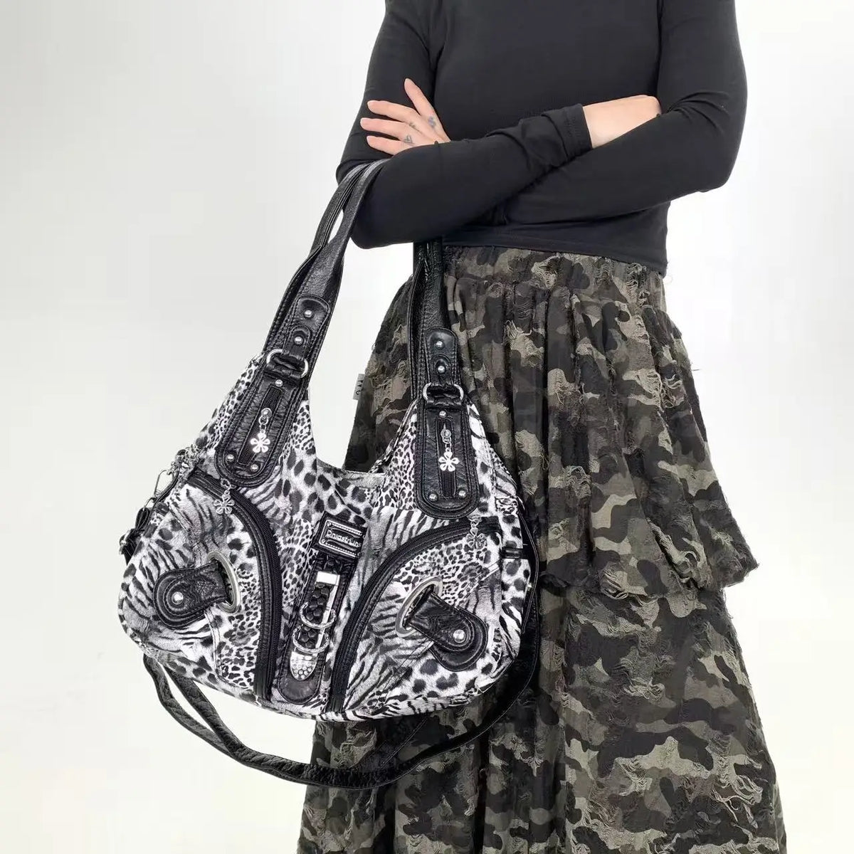 A woman wearing a black top and camouflage skirt holds a leopard print crossbody shoulder bag.