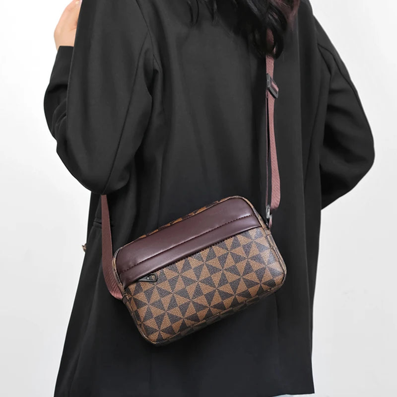 A brown patterned PU leather shoulder bag with a wide strap is carried by a person wearing a black coat.