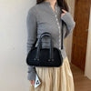 A woman wearing a grey knit sweater and light skirt holds a black crocodile textured mini crossbody bag.