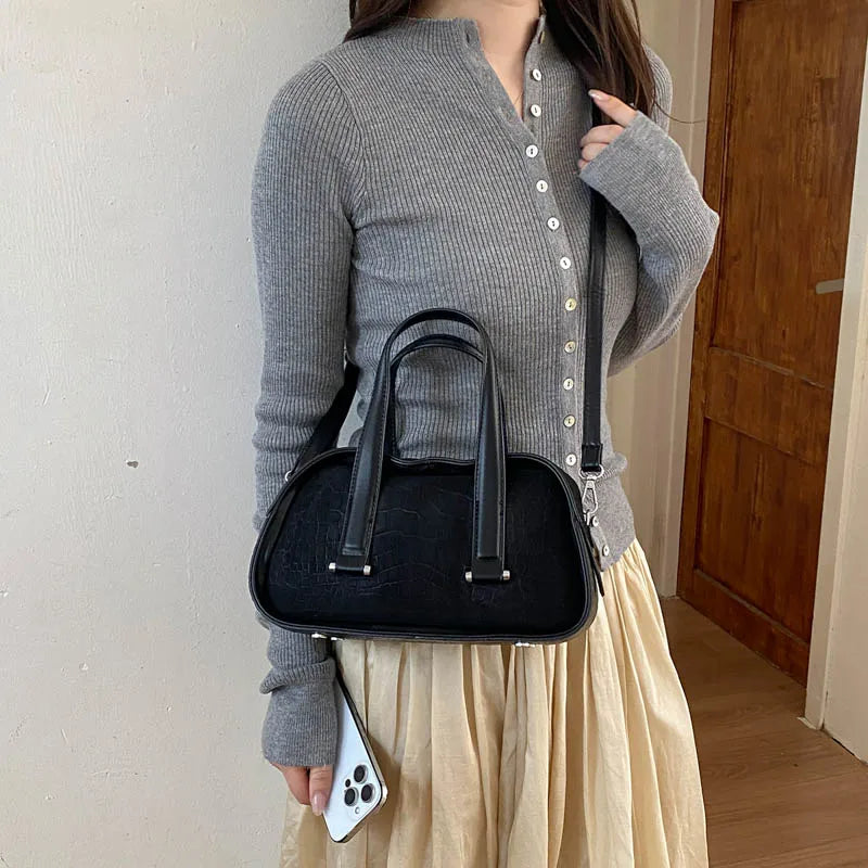 A woman wearing a grey knit sweater and light skirt holds a black crocodile textured mini crossbody bag.