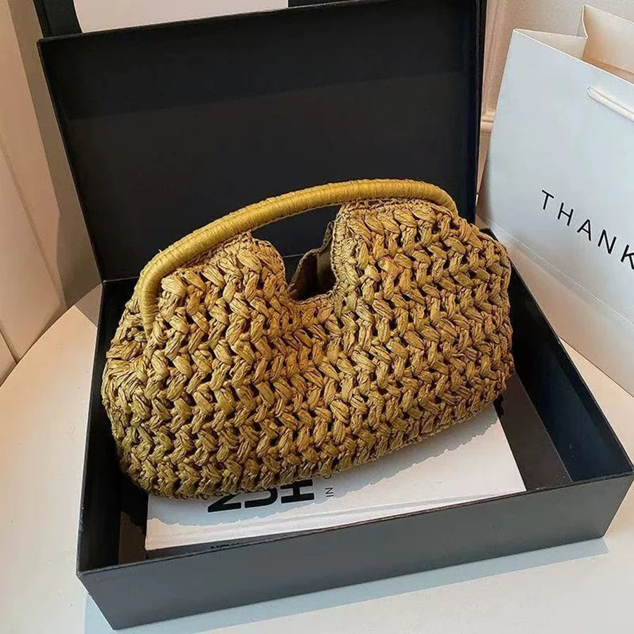 Pochette à fermeture automatique en fibre naturelle tissée, couleur brun doré, présentée dans une boîte noire.