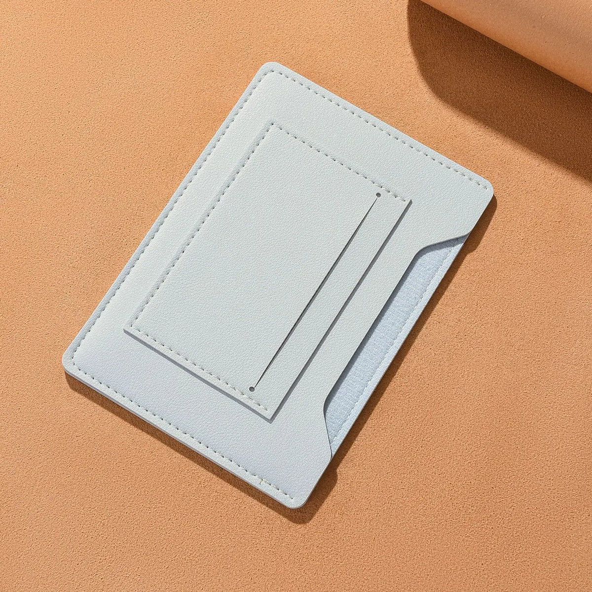 Portefeuille de voyage fin bleu clair pour passeport et documents, posé sur une surface beige.