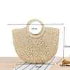 A beige handwoven straw moon bag with a top handle shown on a wooden surface.