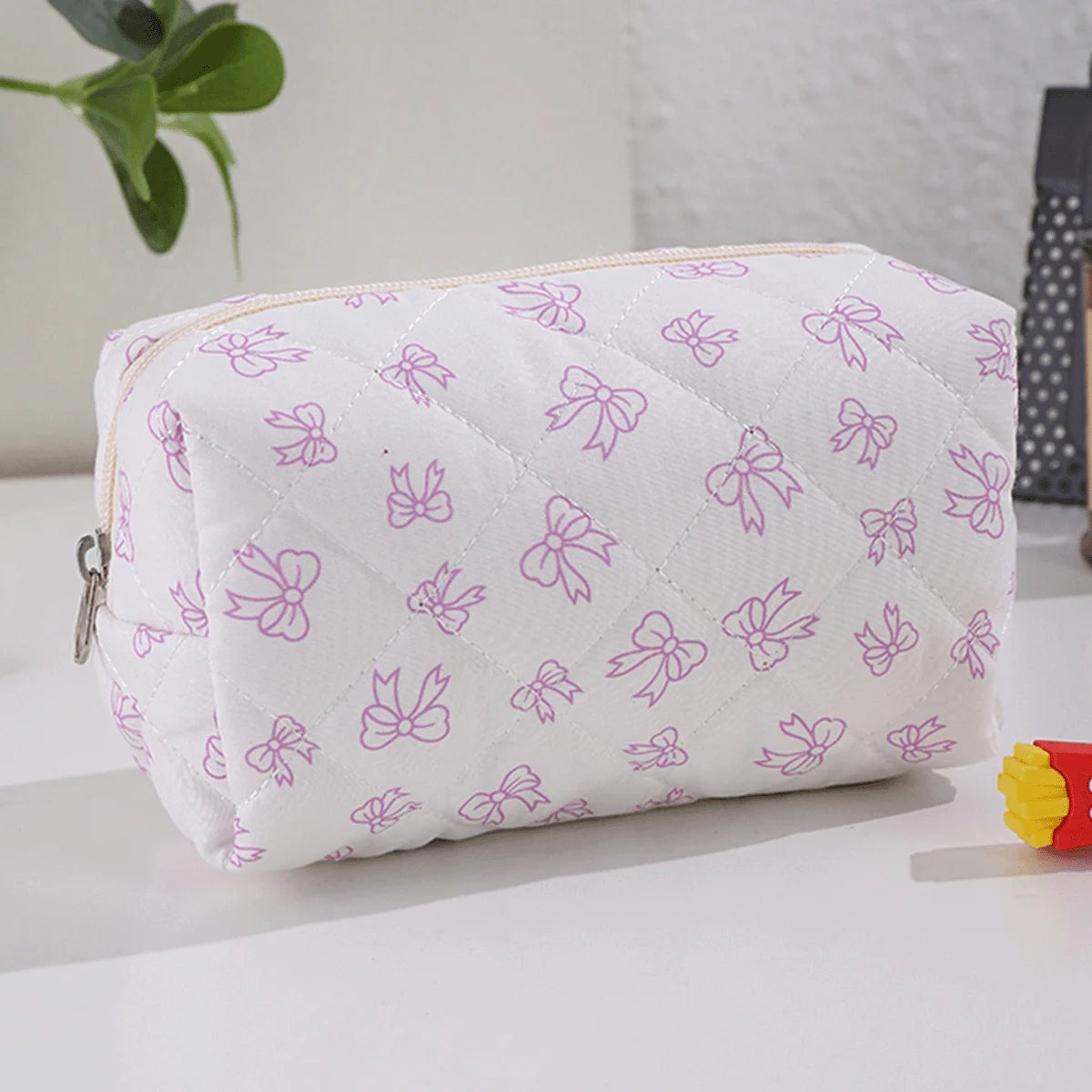 Bolsa acolchada blanca para maquillaje con estampado de lazo morado claro.