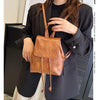 Une femme portant un blazer noir tient un petit sac à dos en cuir marron rétro à cordon.