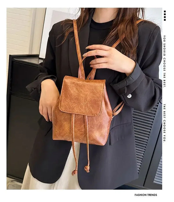 Eine Frau trägt einen schwarzen Blazer und hält einen retro braunen Leder-Zuggriff-Mini-Rucksack.