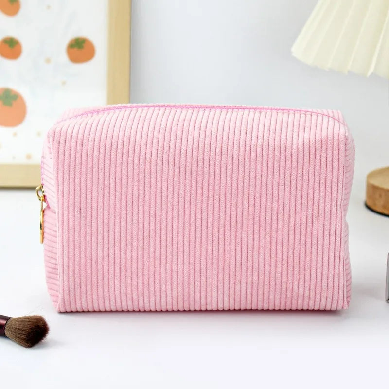 A pink corduroy makeup organizer bag with a vertical ribbed texture resting on a white surface.