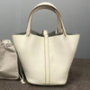 A cream-colored genuine leather bucket bag with a light beige interior lining is shown on a dark surface.