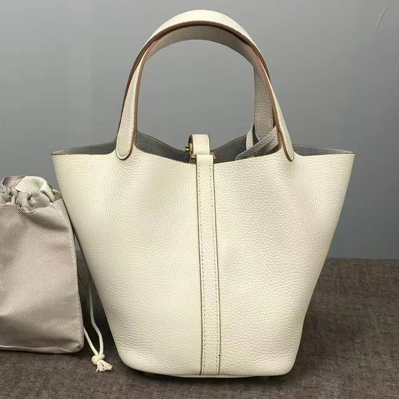 A cream-colored genuine leather bucket bag with a light beige interior lining is shown on a dark surface.