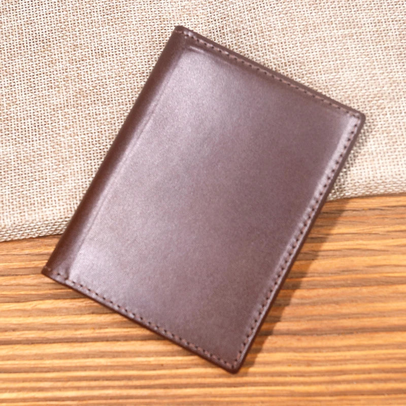 A brown genuine leather bifold card holder resting on a wooden surface.