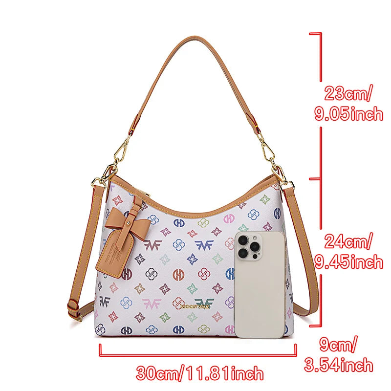 A beige crescent tote bag featuring a letter print and a bow accent, shown with dimensions.