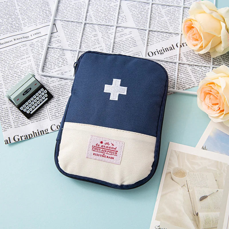 A navy blue pouch containing a white cross first aid kit rests on a light blue surface next to some papers and roses.
