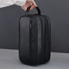 A black premium PU leather toiletry bag being held by a hand against a gray background.