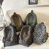 A collection of five leopard print canvas backpacks displayed on a light-colored sofa.