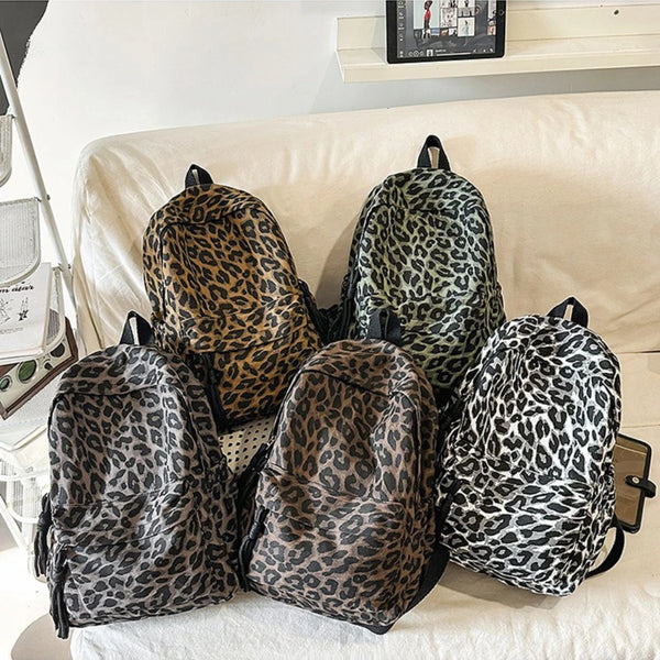 A collection of five leopard print canvas backpacks displayed on a light-colored sofa.