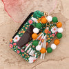 Cartera de silicona floral verde con cremallera y llavero de cuentas blancas, naranjas y verdes.