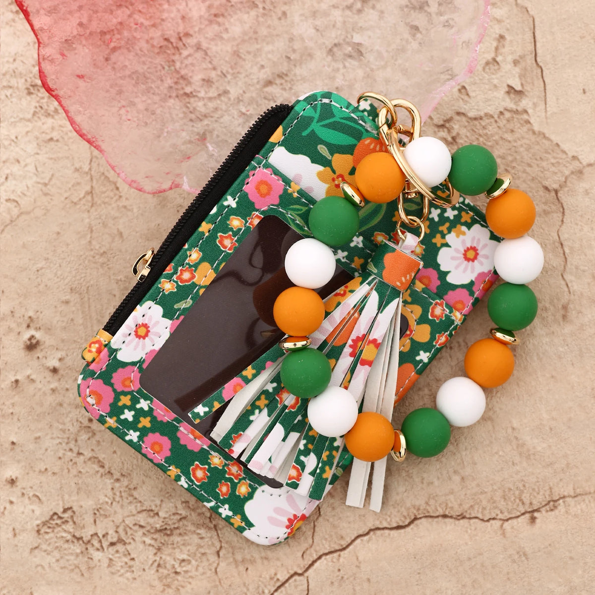 Cartera de silicona floral verde con cremallera y llavero de cuentas blancas, naranjas y verdes.