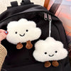 A white cloud shaped plush keychain with brown feet is attached to a black backpack.