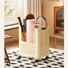 A cream-colored foldable laundry basket with mesh detailing is shown on a wooden floor next to a window.
