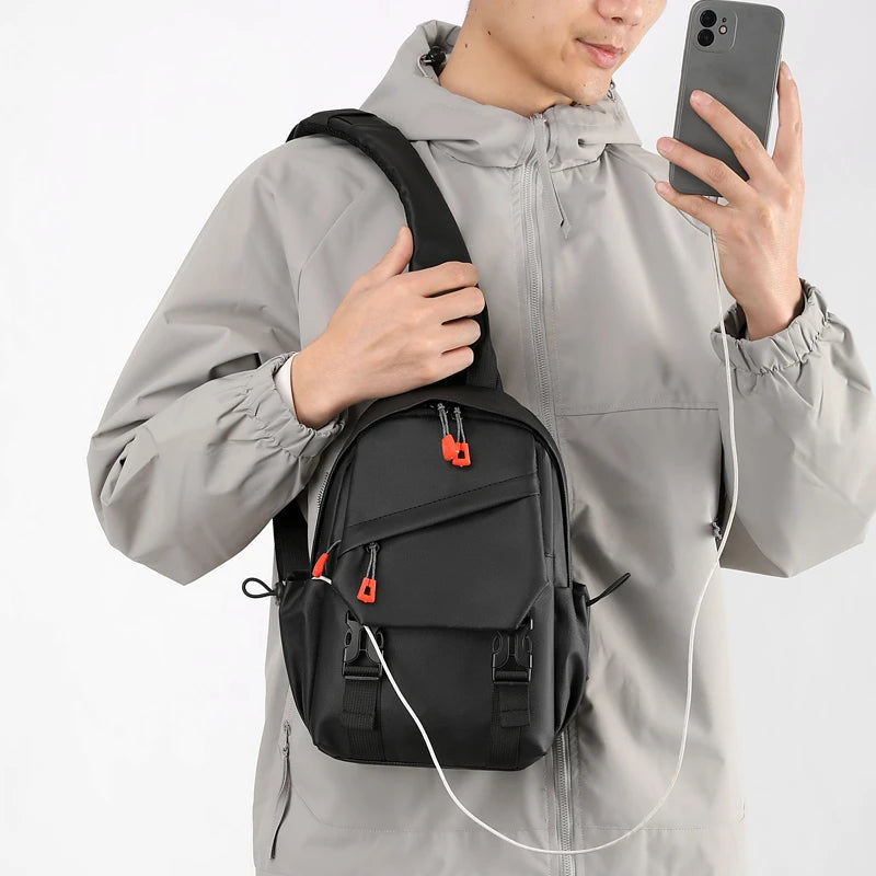 Un homme portant une veste grise tient un sac de sport noir et un câble de charge blanc.