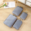 A set of four gray travel compression packing cubes lying on a light wooden surface next to an open book.