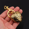 A gold-toned leopard print heart charm keychain is held in a person's hand against a dark background.