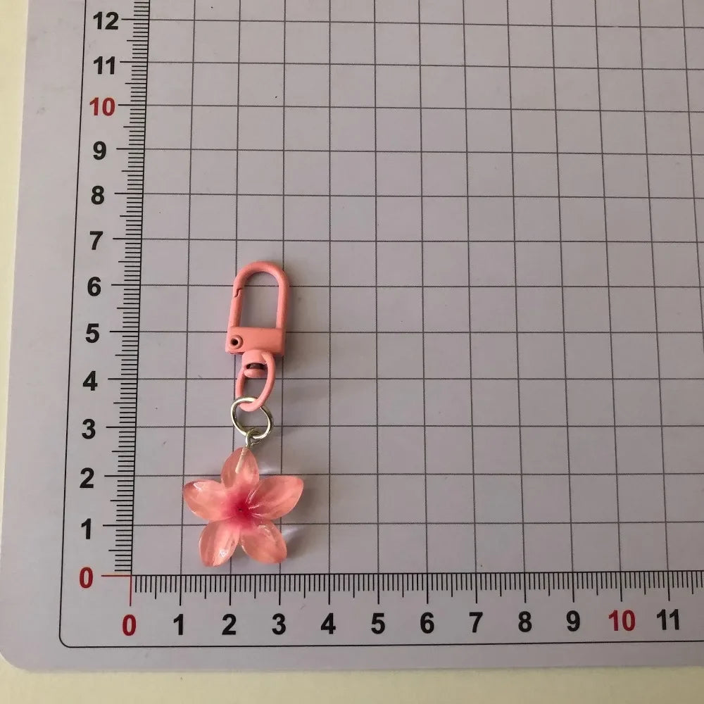 A pink resin flower keychain with a silver jump ring attached, measured against a ruler.