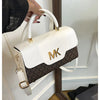 A white Michael Kors classic letter square crossbody bag with gold hardware being held by a hand.