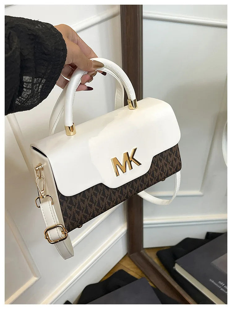 A white Michael Kors classic letter square crossbody bag with gold hardware being held by a hand.