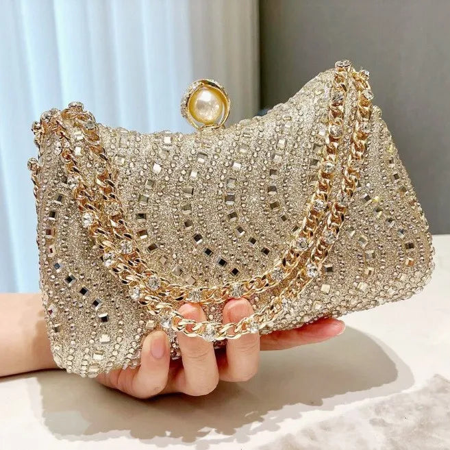 A close-up of a gold and diamond rhinestone clutch bag being held by a hand.